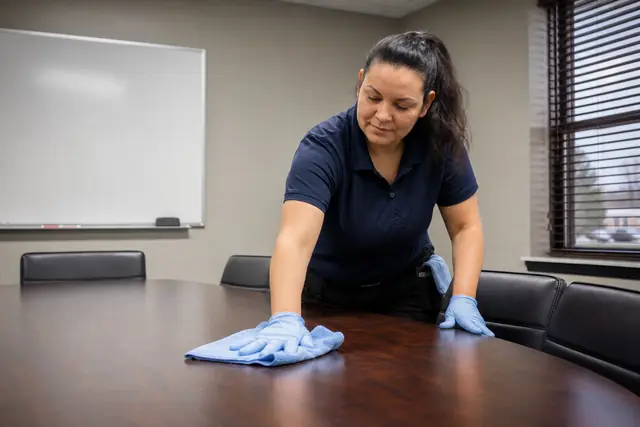 Cleaner in gloves wiping down an office conference table