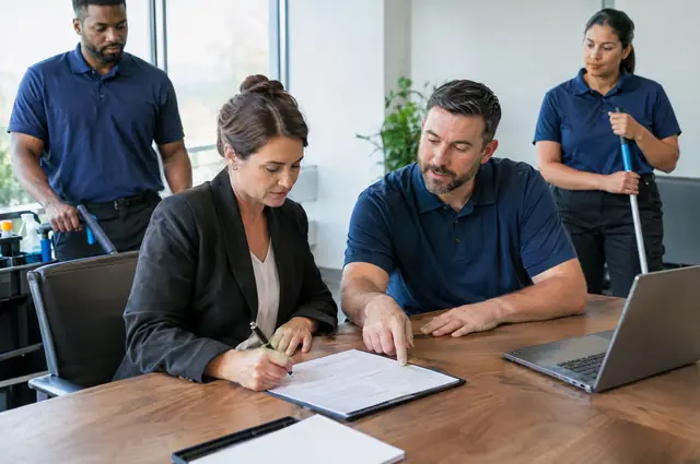 Office manager reviewing a printed cleaning service agreement at a desk with a cleaner in the background